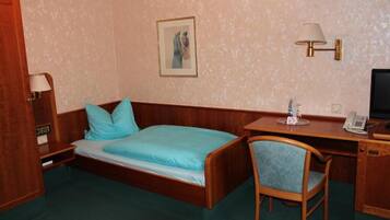 Ein Zimmer mit Bett, Schreibtisch, Stuhl, Lampe, Telefon und einem Bild an der Wand.