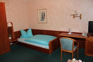 A room with a bed, a desk, a chair, a lamp, a telephone, and a picture on the wall. - Gästehaus Wild (Oberasbach)