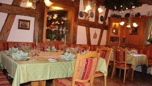 A dining area with a long table set for a meal, wooden chairs, and a rustic interior with exposed beams and a green tablecloth. - Gästehaus Wild (Oberasbach)
