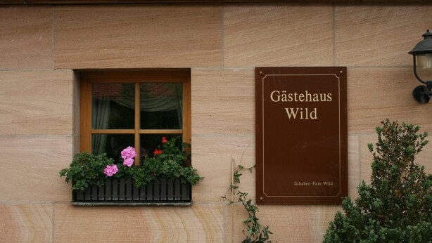 A building with a window displaying pink flowers and a sign reading "Gästehaus Wild". - Gästehaus Wild (Oberasbach)