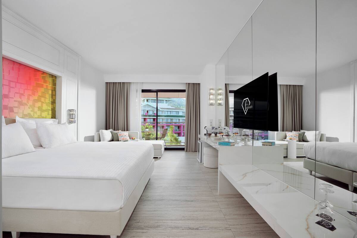 Une chambre d’hôtel moderne avec un grand lit, un coin salon équipé d’un téléviseur et une vue sur un immeuble par la fenêtre.