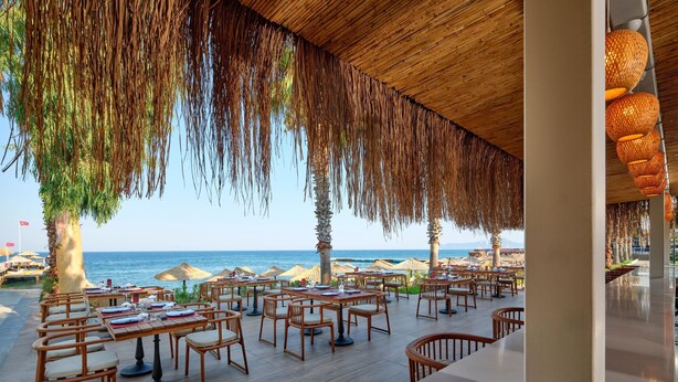 An outdoor dining area with tables and chairs, a view of the sea, and palm trees. - FashionTV Luxe Resort - Luxury All Inclusive (Kemer)