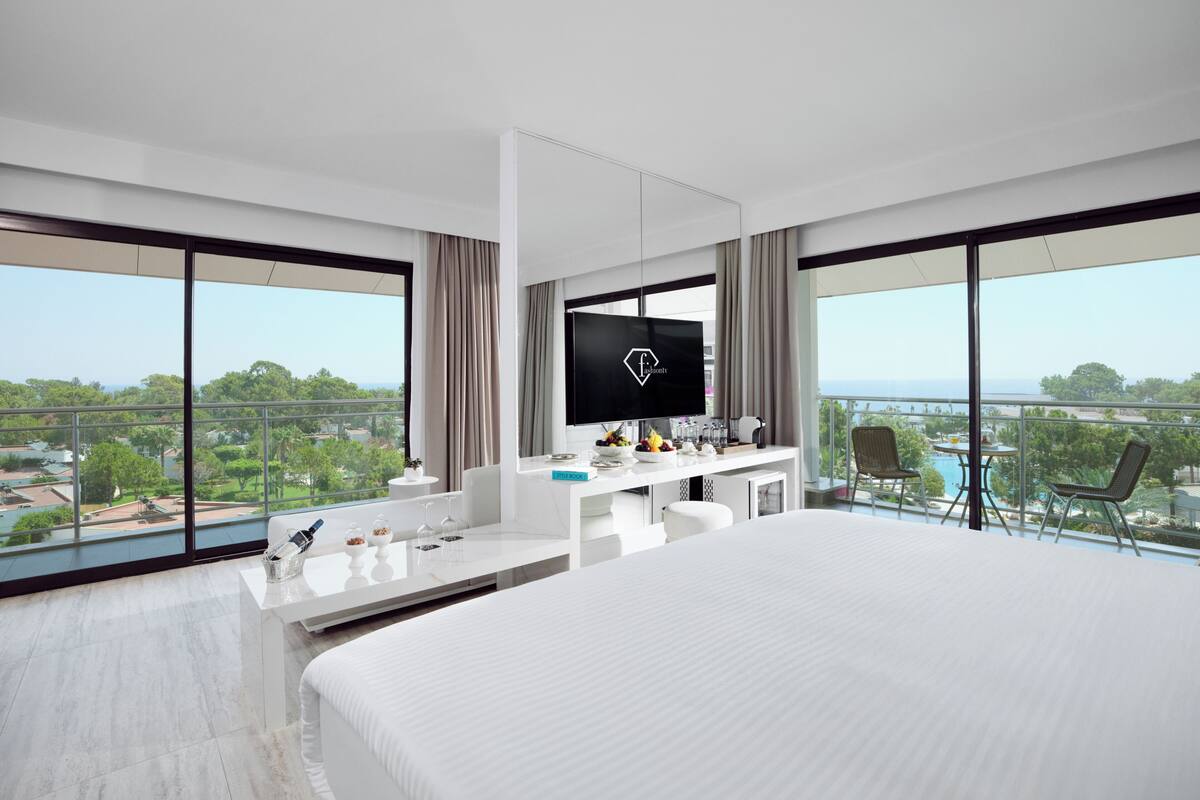 Une chambre d’hôtel moderne dotée d’un grand lit, d’une télévision, d’un balcon avec vue sur la piscine et d’un coin repas.