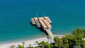 An aerial view of a beachside resort with thatched-roof cabanas, a pier extending into the sea, and a sandy beach with palm trees. - FashionTV Luxe Resort - Luxury All Inclusive (Kemer)