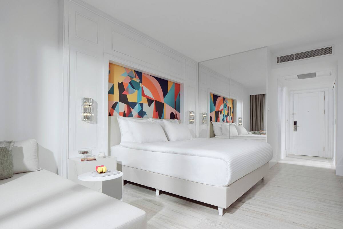 Une chambre d’hôtel moderne avec un grand lit, une table de chevet et une peinture abstraite aux couleurs vives accrochée au mur.