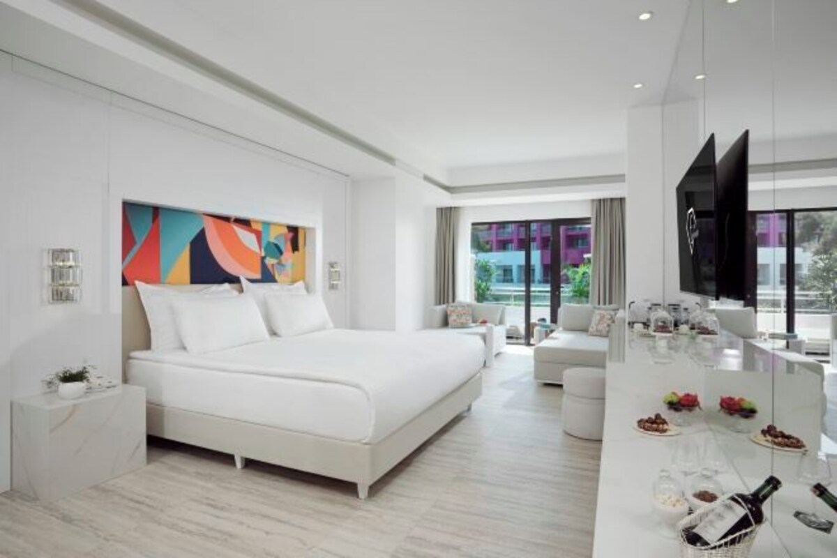 A modern hotel room with a large bed, a dining area, and a TV.