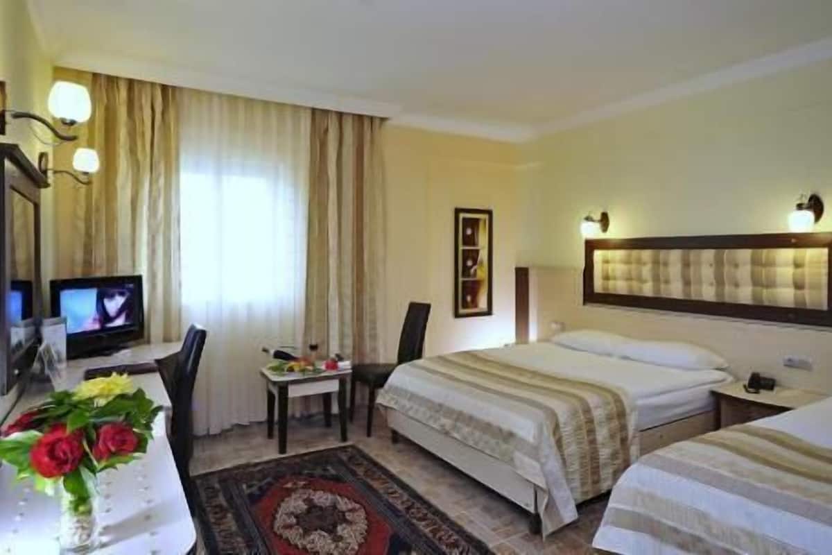 A hotel room with two beds, a desk with a computer, a chair, a desk lamp, a framed picture, and a window with curtains.