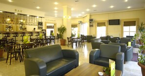 Eine großzügige Lobby mit Bar und Restaurantbereich, verschiedenen Sitzgelegenheiten wie Sofas und Stühle, sowie Zimmerpflanzen.