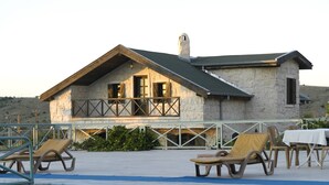 Una casa de piedra con balcón, piscina y sillones de descanso.