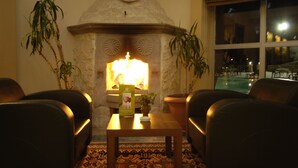 Un rincón tranquilo con chimenea de piedra, dos sillones de cuero, una mesa con la carta de bebidas y vistas a una piscina exterior a través de un ventanal amplio.