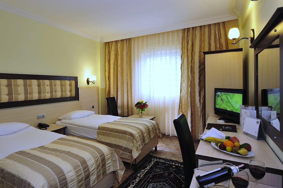 A hotel room with two beds, a desk with a computer, a chair, a small table with fruit, and a mirror.