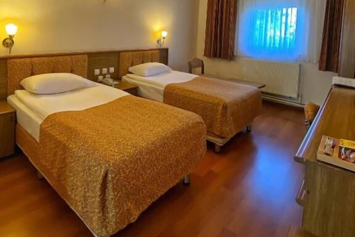 A hotel room with two single beds, a desk, and a window with curtains.