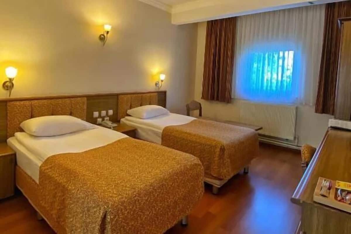A hotel room with two beds, a desk, and a window with curtains.