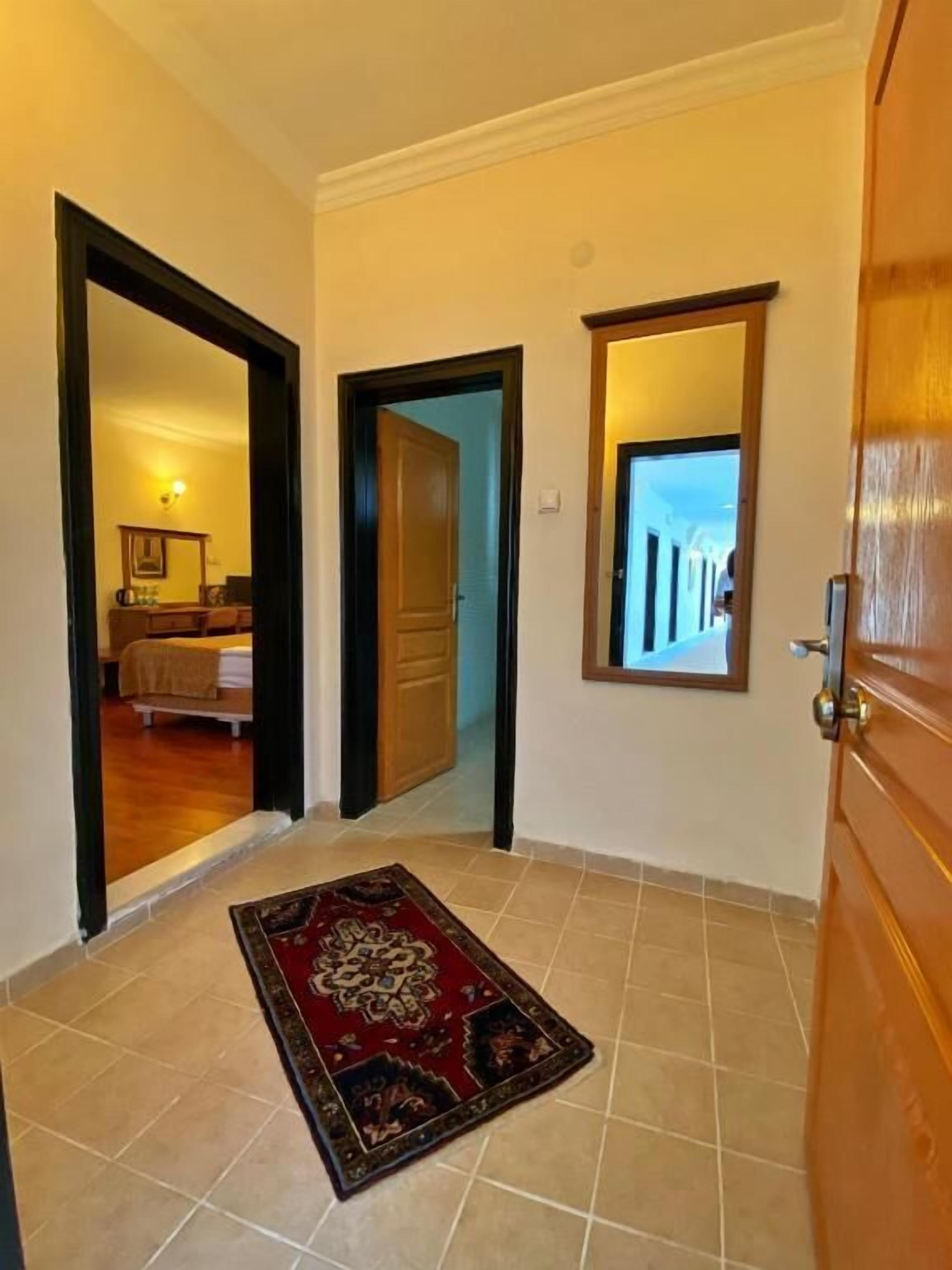 A hallway with a wooden door, a mirror, and a red patterned rug on the floor.