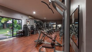 Une salle de sport équipée de divers appareils d’exercice, dotée de grandes fenêtres et d’un plancher en bois.
