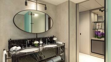 A modern bathroom with a large oval mirror, two sinks, and a vanity with a marble countertop.