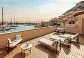 A rooftop terrace with lounge chairs, a table, and a view of a marina with boats.