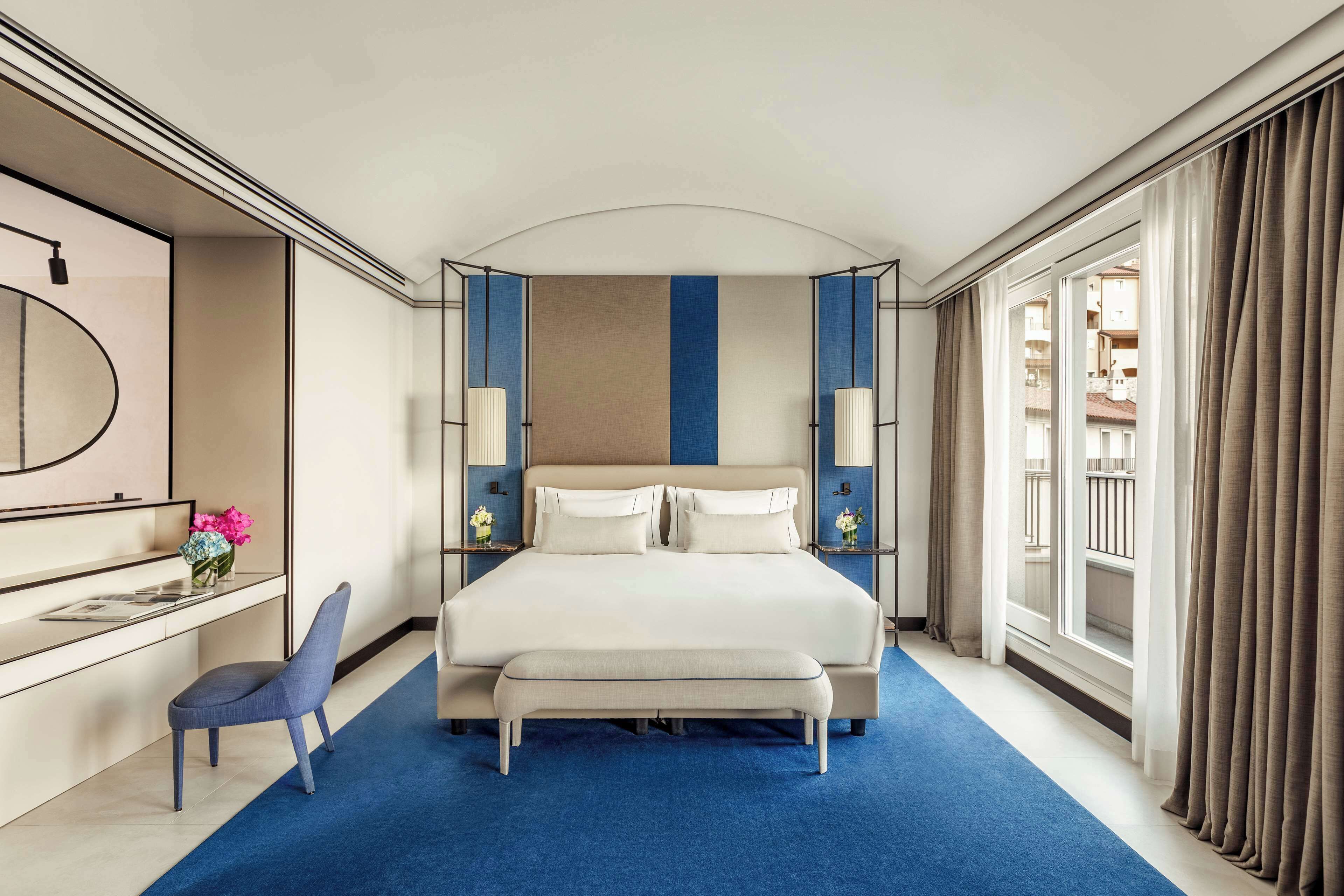 Ein Hotelzimmer mit einem großen Bett, einem Schreibtisch mit Stuhl, einem Spiegel und Blick ins Freie.