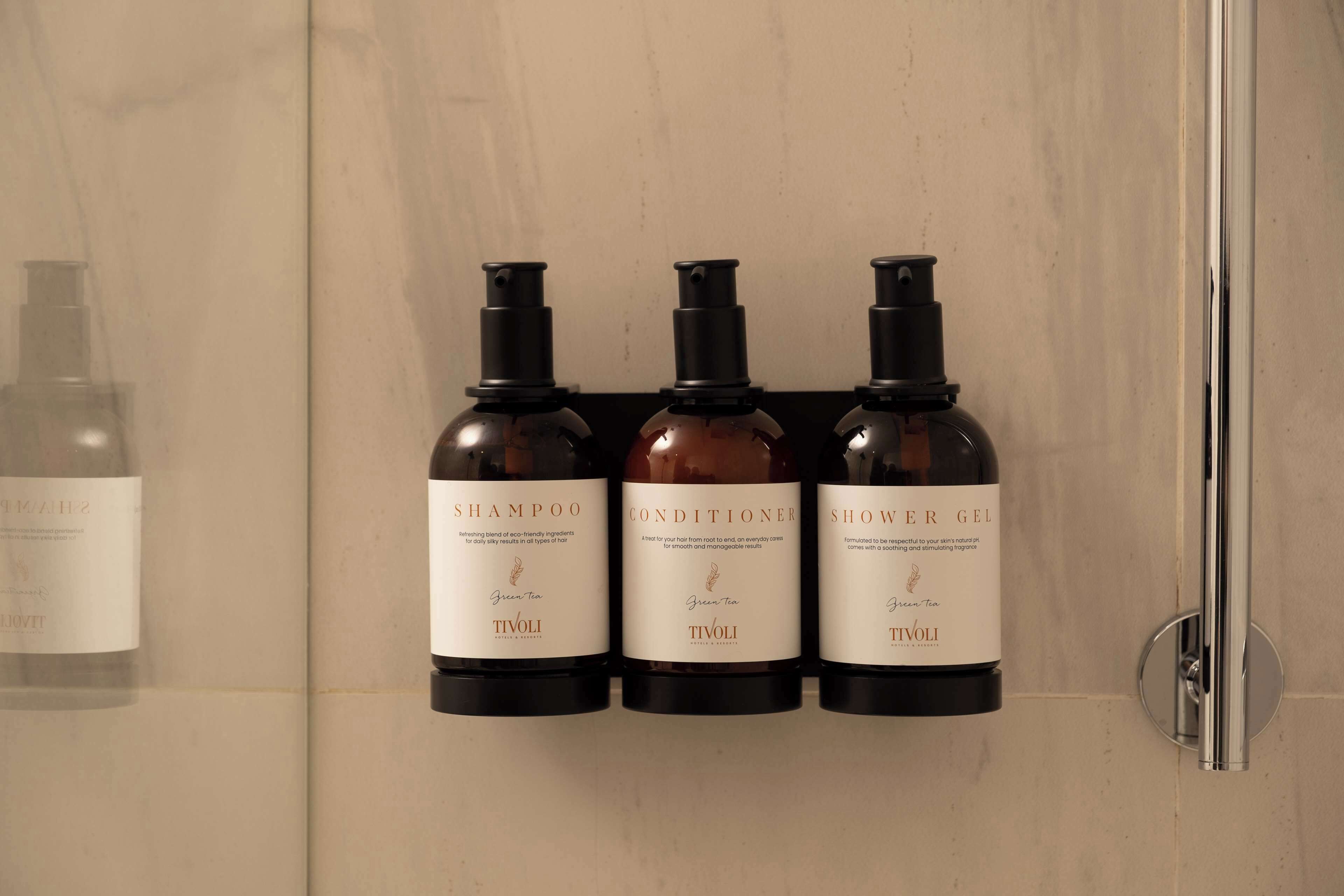 Three bottles of green tea-based products on a wall-mounted holder in a bathroom.