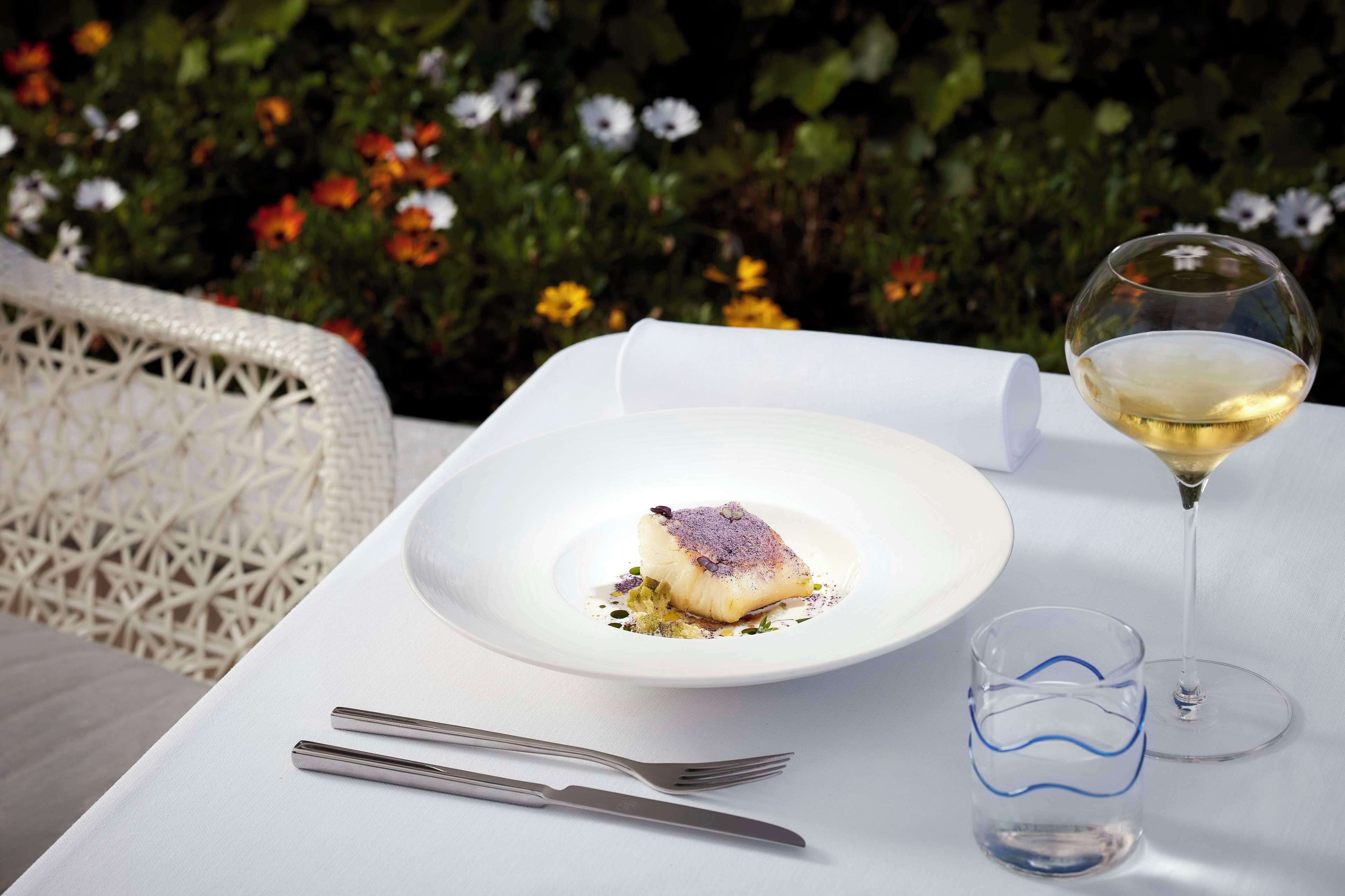 Une table à manger avec une assiette blanche, un verre de vin blanc et une fourchette.
