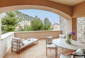 A balcony with a wooden floor, a lounge chair, a dining table, and a view of buildings and trees.