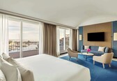 A hotel room with a large bed, a sofa, a TV, and a balcony with a view.