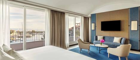 A hotel room with a large bed, a sofa, a TV, and a balcony with a view.