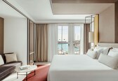 A hotel room with a large bed, a sofa, a coffee table, and a view of the sea through a glass door.