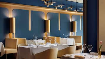 Un restaurante con mesas dispuestas para comer, iluminación colgante y una pared azul con paneles de madera.