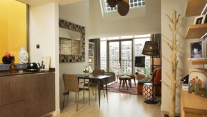 Een moderne woonruimte met een keuken, een eethoek en een zithoek. Er is een groot raam dat natuurlijk licht en stadszicht biedt.