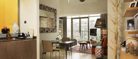 A modern living space with a kitchen, dining area, and seating area. There is a large window providing natural light and a view of the city.