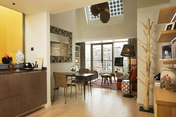 Un espace de vie moderne comprenant une cuisine, un coin repas et un coin salon. Une grande fenêtre offre une lumière naturelle et une vue sur la ville.