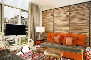 Una sala de estar moderna con un sofá, un televisor y vistas de la ciudad a través de amplios ventanales.