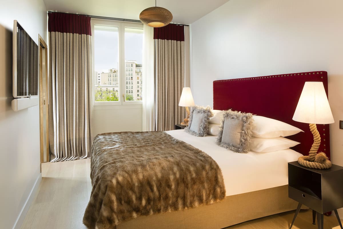 Una habitación de hotel con una cama grande, dos lámparas de noche, un televisor y una ventana con cortinas.