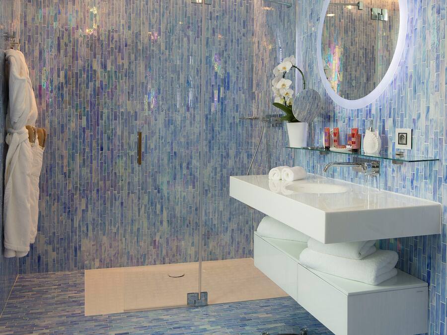 A modern bathroom with a glass vanity, a large mirror, and a shower area.