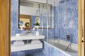 Un baño moderno con cabina de ducha de vidrio, tocador blanco con espejo y salpicadero de mosaico azul.