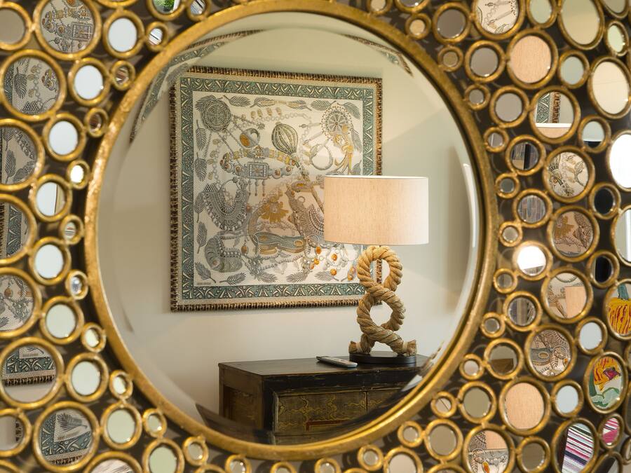 A mirror with a decorative frame and a lamp on a dresser.