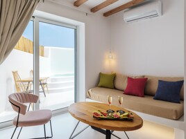 Una sala de estar moderna con una mesa de madera, dos sillas, un sofá con cojines coloridos y un balcón con cerramiento de madera.