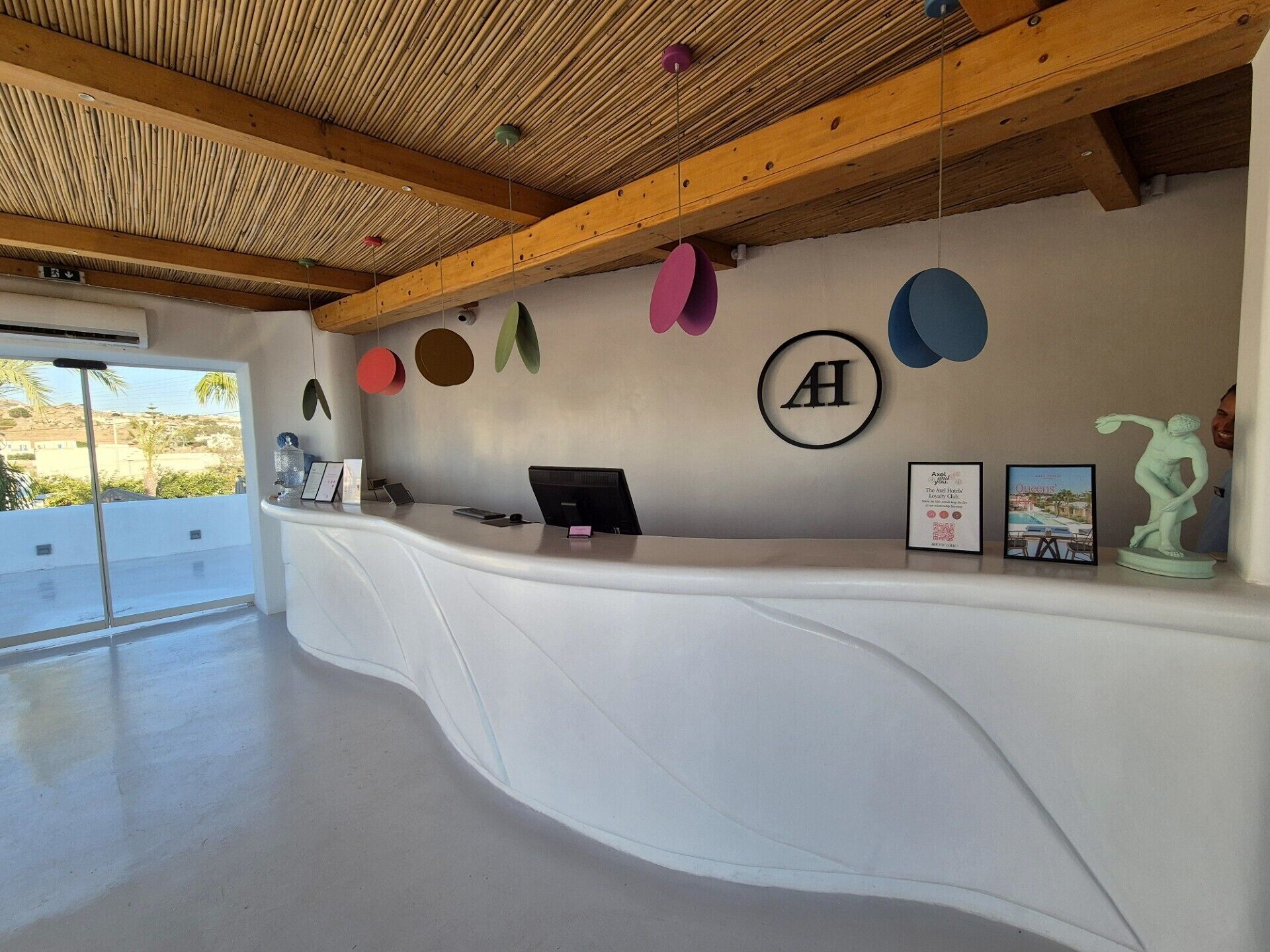 A reception desk with a modern design, featuring a wooden ceiling and a large window offering a view of the outdoors.