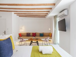 Quarto de hotel moderno com teto de madeira, um conjunto de sofás, uma mesa de jantar e uma televisão de tela plana na parede.