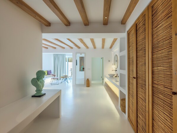 Un interior moderno con un banco blanco, vigas de madera, un espejo grande y una cesta de mimbre.