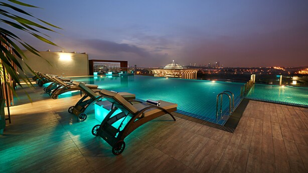Un espace piscine aménagé sur le toit, avec des chaises longues et une vue sur les toits de la ville au crépuscule.