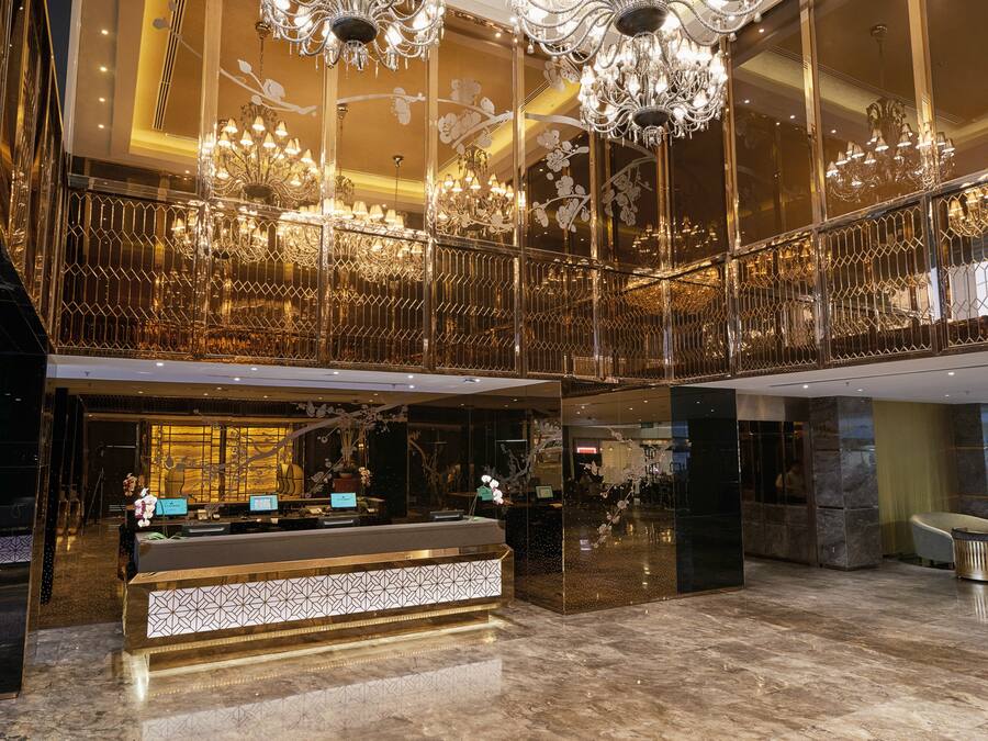 A luxurious hotel lobby with a grand reception desk, ornate chandeliers, and a spacious balcony area.