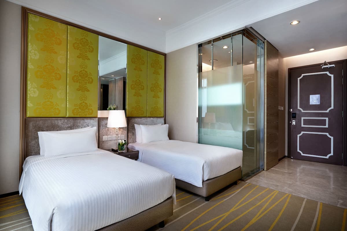 Hotelkamer met twee bedden, een grote spiegel, een glazen scheidingswand en een deur met een geometrisch ontwerp.