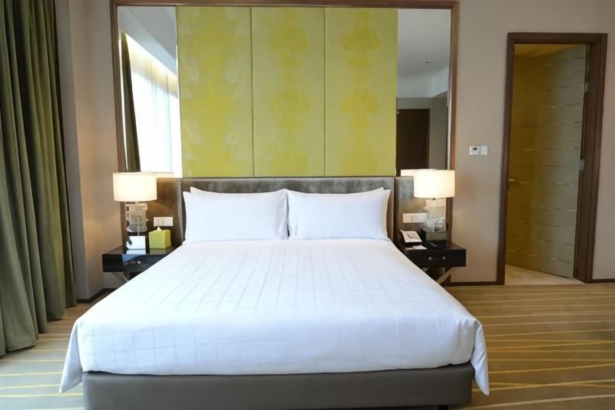 A hotel room with a large bed, two bedside tables with lamps, a mirror above the bed, and a door to the right.