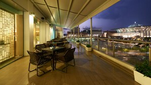 Un restaurant avec des tables et des chaises, une vue sur le paysage urbain et une grande fenêtre donnant sur une étendue d’eau.