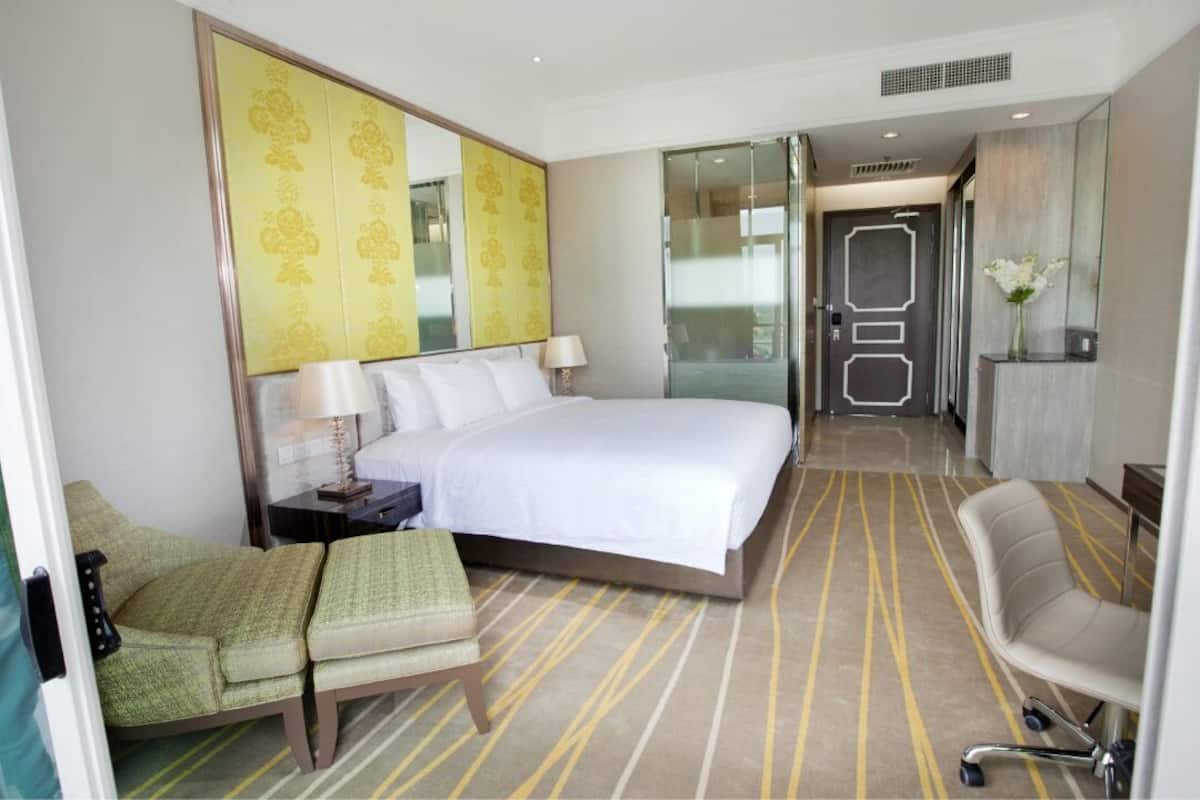 Een hotelkamer met een bed, twee stoelen, een nachtkastje, een lamp, een spiegel en een deur naar een badkamer.