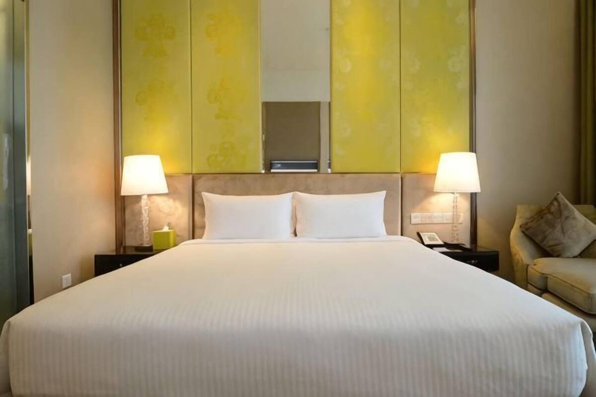 Een hotelkamer met een groot bed, twee bedlampen, een nachtkastje, een bank en een spiegel boven het bed.