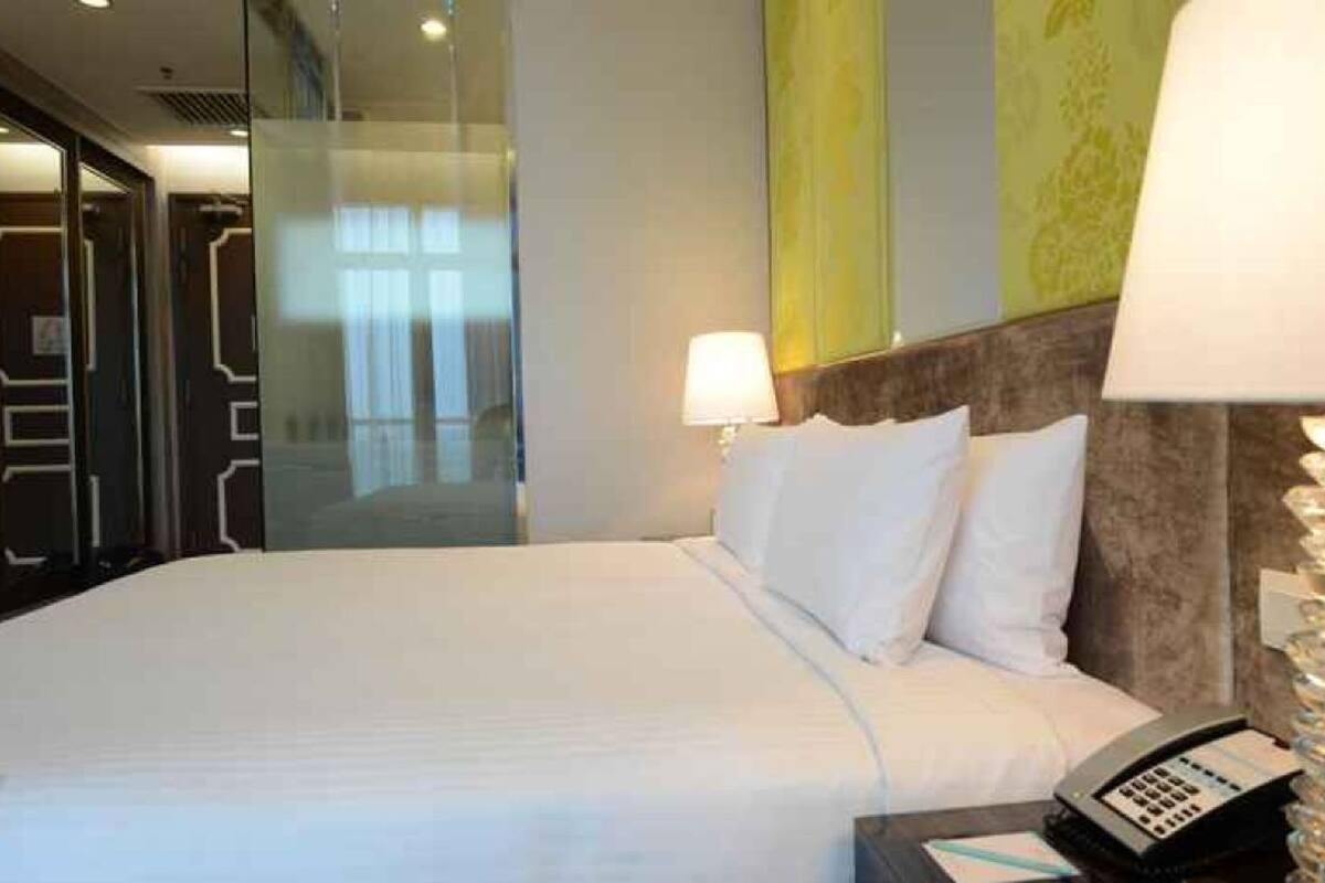 Een hotelkamer met een bed, een bedlampje, een telefoon en een glazen scheidingswand.