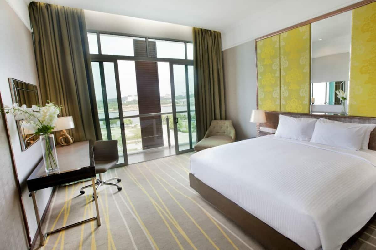 Hotelkamer met een groot bed, een bureau met stoel, een spiegel en uitzicht op een landschap door grote ramen.